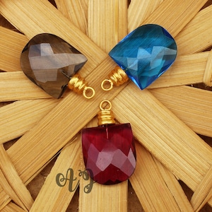 May include: Three gemstone pendants with gold jump rings. The pendants are faceted and have a teardrop shape. The gemstones are smoky quartz, blue topaz, and red garnet.