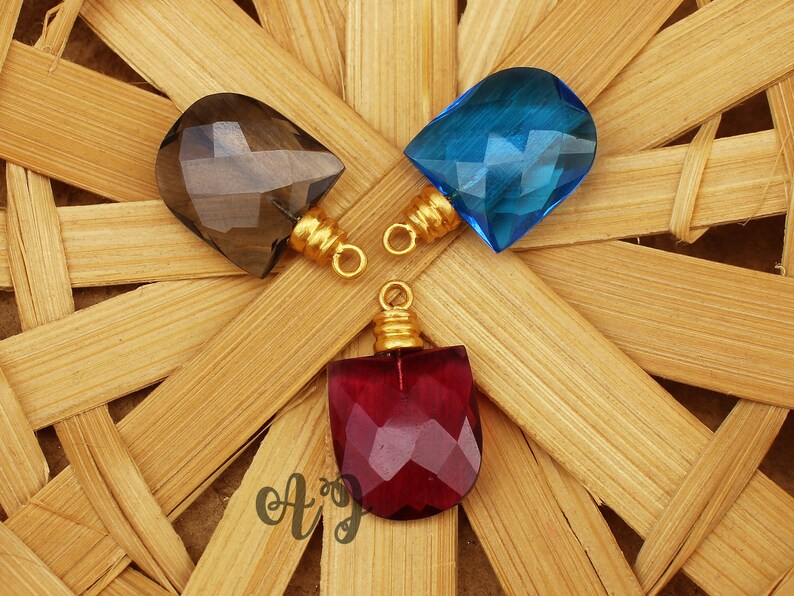 May include: Three gemstone pendants with gold jump rings. The pendants are faceted and have a teardrop shape. The gemstones are smoky quartz, blue topaz, and red garnet.