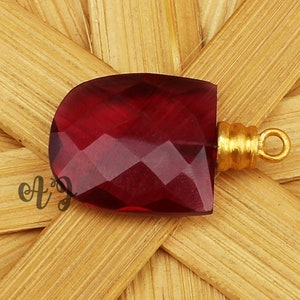 May include: A deep red faceted gemstone pendant with a gold-toned metal bail.