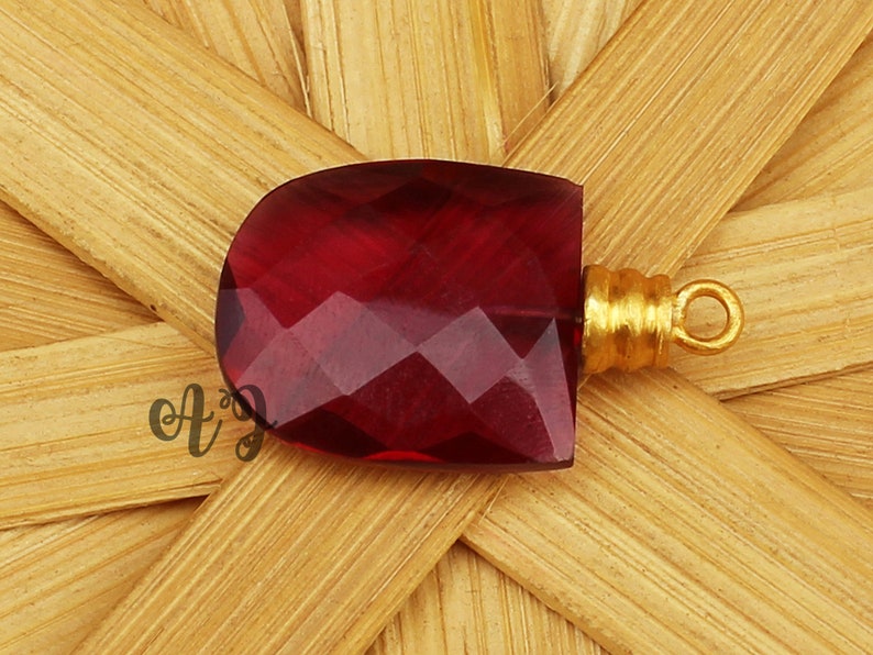 May include: A deep red faceted gemstone pendant with a gold-toned metal bail.