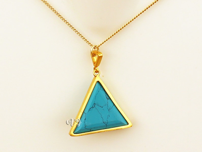 May include: A gold-colored necklace with a triangular pendant. The pendant features a turquoise stone set within a gold frame. The necklace chain is delicate and gold-colored, creating a simple yet elegant design.
