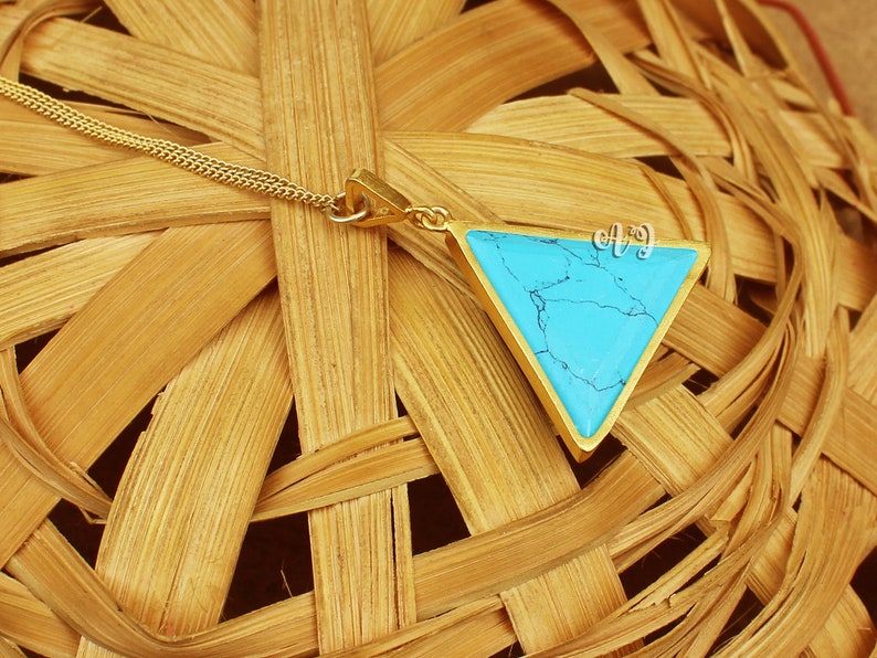May include: A gold-colored necklace featuring a triangular pendant with a vibrant turquoise stone. The pendant is framed by a gold border and hangs from a delicate gold chain. The turquoise stone has a unique, natural pattern.