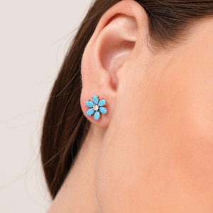 May include: A pair of silver stud earrings featuring a turquoise flower design with a small diamond in the centre.