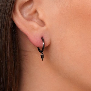 May include: Black hoop earrings with a small triangle pendant hanging from the bottom.