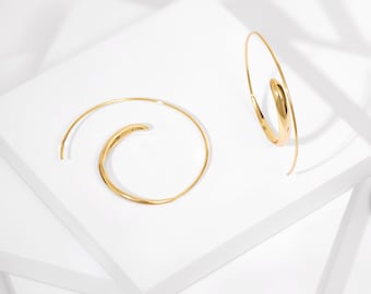 May include: A pair of gold hoop earrings with a unique spiral design. The earrings are made of a smooth, shiny metal and have a modern, minimalist aesthetic.