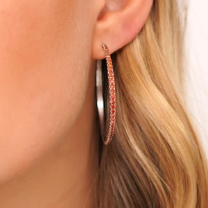 May include: Silver hoop earrings with a row of small orange gemstones around the edge.