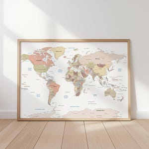 May include: A framed world map in a light wood frame. The map uses a muted colour palette with countries in beige, brown, and green. Oceans are labelled in blue. A decorative piece for home or office, with measurements in centimetres.