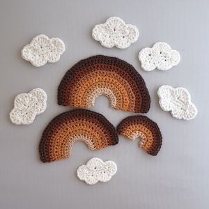 May include: A set of crocheted rainbow and cloud decorations in brown, orange, and white. The rainbow is made of three pieces, and there are six clouds.