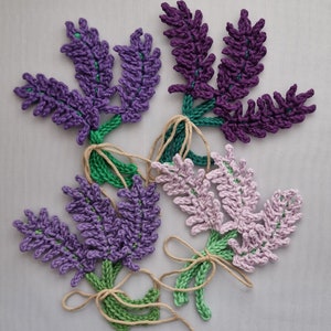 May include: Four crocheted lavender flower sprigs with green stems and brown twine bows. The flowers are purple, pink, and a lighter shade of purple.