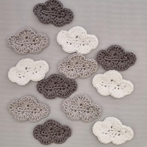 May include: A collection of twelve crocheted cloud shapes in various shades of grey and white. The clouds are arranged in a random pattern on a grey background.