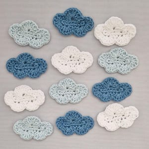 May include: Twelve crocheted cloud shapes in various shades of blue and white. The clouds are arranged in three rows of four.