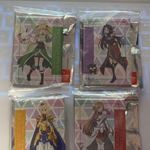 May include: Four packaged collectible cards featuring characters from Sword Art Online and Sanrio. Each card displays a different character in colorful outfits, with the text "SWORD ART ONLINE x Sanrio characters". The cards are in clear plastic packaging.