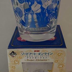 May include: A clear glass featuring blue anime-style character illustrations. The glass is on a blue box with Japanese text and the words "SWORD ART ONLINE ~Project Alicization~". The box also features an illustration of a character.