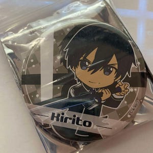 May include: A round button featuring an anime character with black hair and blue eyes. The character is named Kirito, with the name printed in white. The button has a black, white, and gray background and is encased in clear plastic.