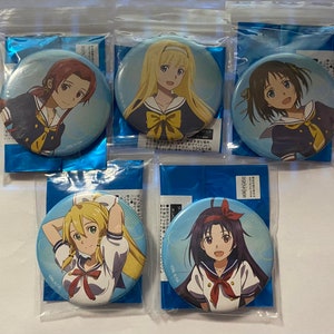 May include: Five round anime character pinback buttons in clear plastic packaging. Each button features a different female character with various hairstyles and school uniforms. The buttons are blue and white with Japanese text.
