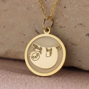 May include: A gold necklace with a round pendant featuring a sloth hanging upside down. The pendant has a smooth, shiny finish.