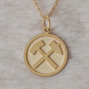 May include: A gold necklace with a round pendant featuring two crossed pickaxes.