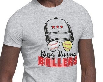 May include: A gray t-shirt with a baseball cap and sunglasses design. The sunglasses are made of baseballs. The text on the shirt reads "Busy Raising Ballers".