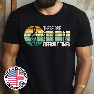 May include: Black t-shirt with a vintage-style graphic of a treble clef and the text "These are difficult times 6 9 4 8 11 16".