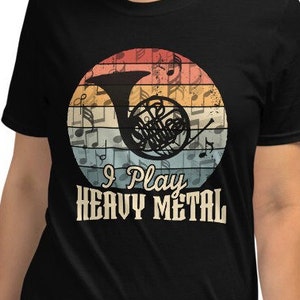 Könnte beinhalten: Ein schwarzes T-Shirt mit einer Grafik im Vintage-Stil eines französischen Horns und Noten. Der Text "I Play Heavy Metal" ist unter der Grafik gedruckt.