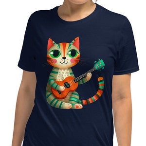May include: A navy blue t-shirt with a colorful illustration of a cat playing a ukulele. The cat has green eyes, orange fur, and a striped tail.