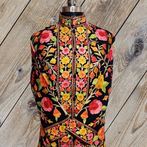 May include: A long black embroidered jacket with a high collar and floral embroidery in shades of pink, orange, yellow, and green.