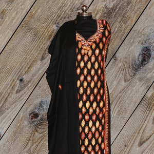 May include: Black embroidered dress with a long sleeve and a matching shawl. The embroidery is in shades of orange, yellow, and white. The dress has a V-neckline and a straight silhouette. The shawl is draped over the shoulders and has a fringe trim.