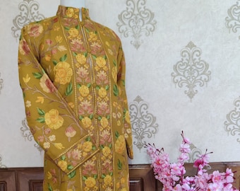 May include: A long, mustard yellow embroidered jacket with a floral pattern. The jacket has a mandarin collar and a button closure. The embroidery is in shades of yellow, pink, and green.