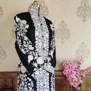 May include: A long black coat with white floral embroidery. The coat has a high collar and long sleeves. The embroidery is intricate and detailed.