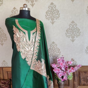 May include: A green silk dress with gold embroidery featuring a floral and bird design. The dress is displayed on a mannequin and has a scoop neckline.