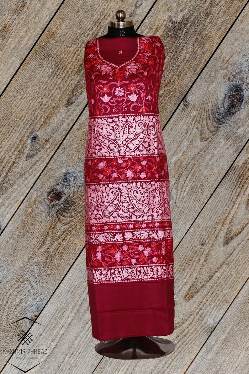 May include: A maroon embroidered dress with pink floral and paisley patterns. The dress is on a mannequin against a wooden background.