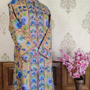 May include: A long, beige embroidered coat with a mandarin collar and floral patterns in shades of blue, green, and pink.