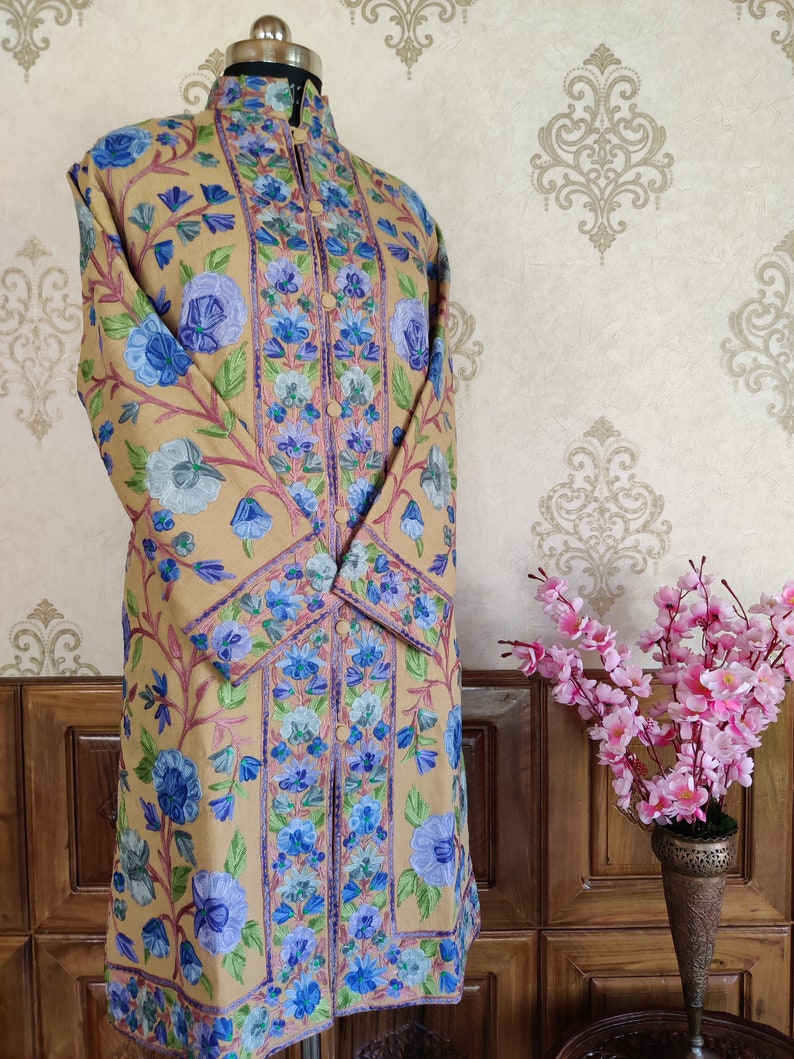 May include: A long, beige embroidered coat with a mandarin collar and floral patterns in shades of blue, green, and pink.