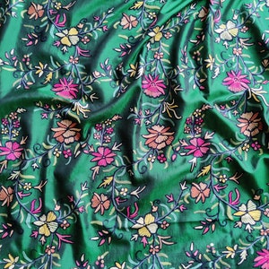 May include: Green fabric with a floral embroidery pattern. The flowers are in shades of pink, orange, yellow, and white.