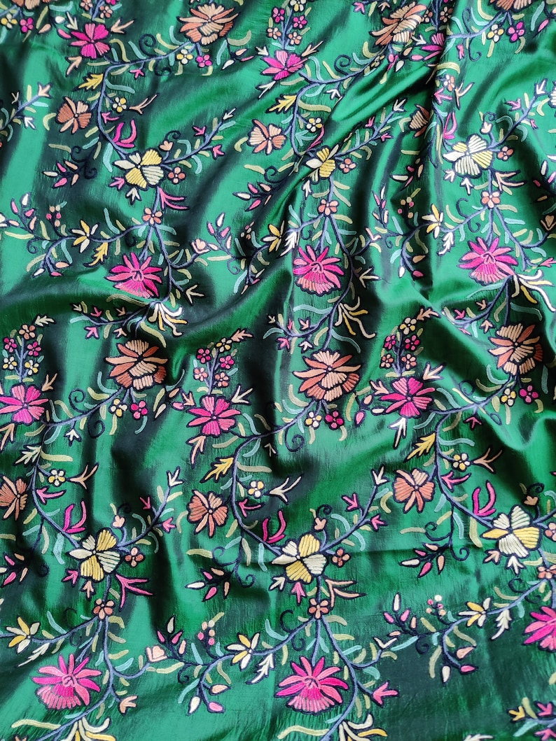 May include: Green fabric with a floral embroidery pattern. The flowers are in shades of pink, orange, yellow, and white.