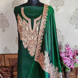 May include: A green silk dress with gold embroidery. The dress has a high neckline and a long, flowing skirt. The embroidery is intricate and detailed, featuring floral and paisley motifs.