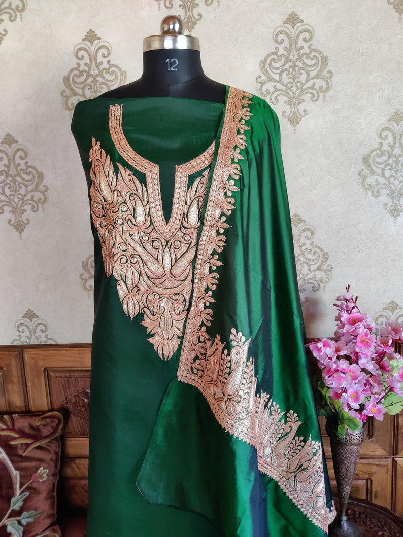 May include: A green silk dress with gold embroidery. The dress has a high neckline and a long, flowing skirt. The embroidery is intricate and detailed, featuring floral and paisley motifs.