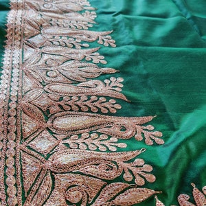 May include: A green fabric with a gold embroidered border. The border features a floral design with intricate details.