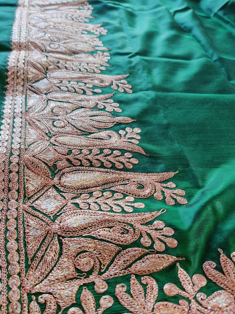 May include: A green fabric with a gold embroidered border. The border features a floral design with intricate details.