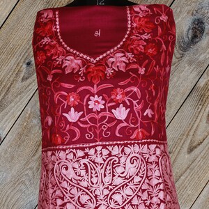 May include: A maroon embroidered fabric with pink floral designs. The fabric has a paisley pattern at the bottom.