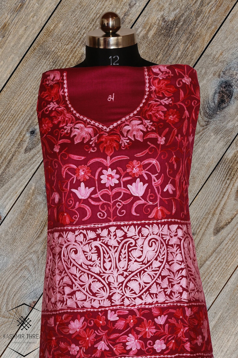 May include: A maroon embroidered fabric with pink floral designs. The fabric has a paisley pattern at the bottom.