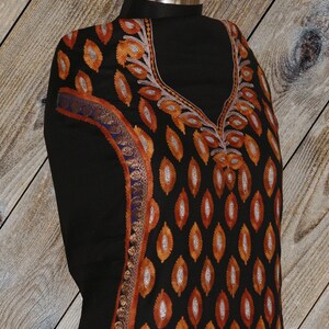 May include: Black fabric with intricate embroidery in orange, silver, and blue. The embroidery features a repeating pattern of leaves and a floral design around the neckline.