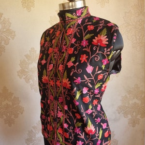 May include: A black sleeveless vest with a high collar and floral embroidery in shades of pink, red, and green.
