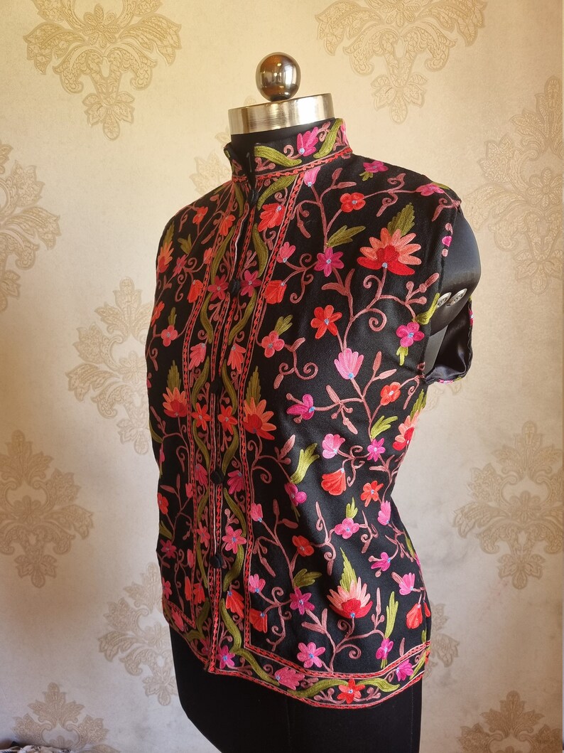 May include: A black sleeveless vest with a high collar and floral embroidery in shades of pink, red, and green.