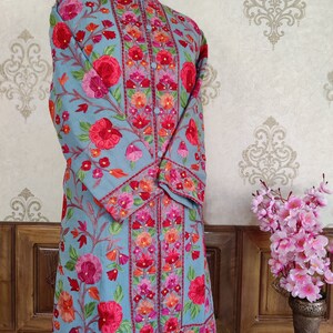 May include: A long, light blue embroidered tunic with a mandarin collar and floral embroidery in shades of pink, red, orange, and green.