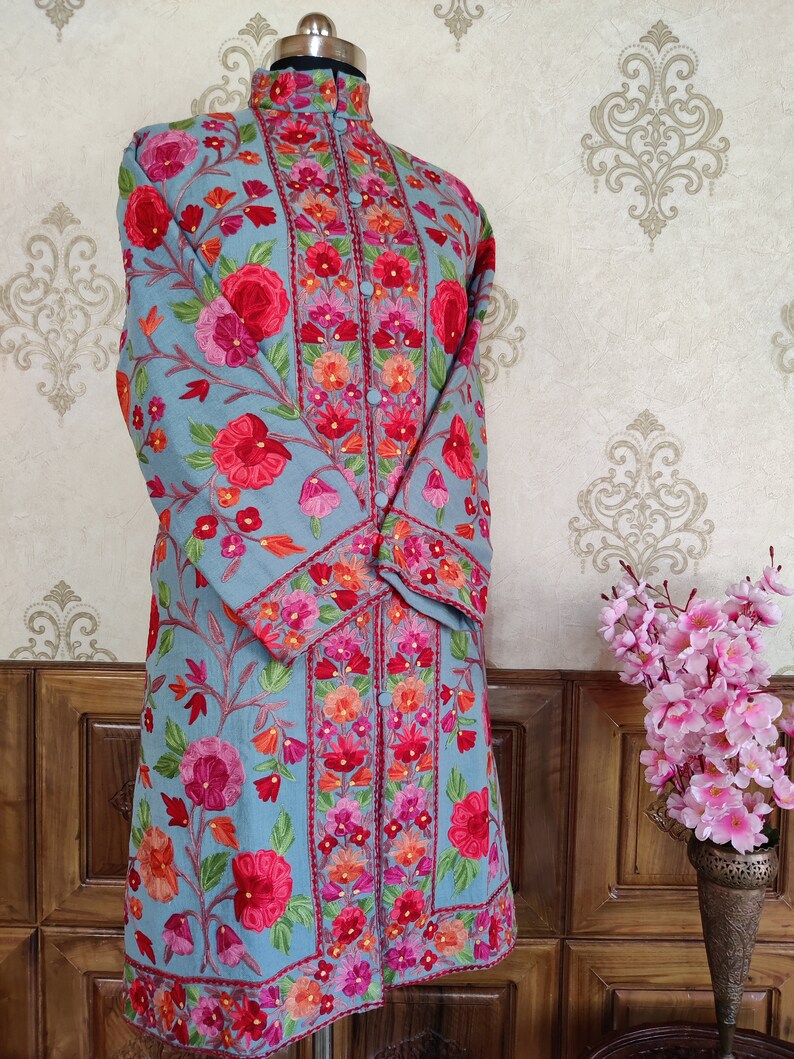 May include: A long, light blue embroidered tunic with a mandarin collar and floral embroidery in shades of pink, red, orange, and green.