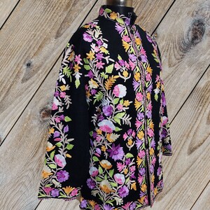 May include: A black embroidered jacket with a floral design in shades of pink, purple, orange, and green. The jacket has a mandarin collar and a long, flowing silhouette.