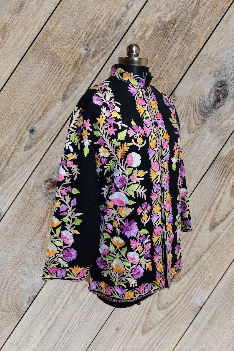 May include: A black embroidered jacket with a floral design in shades of pink, purple, orange, and green. The jacket has a mandarin collar and a long, flowing silhouette.