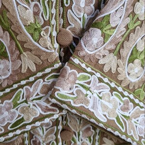 K&ouml;nnte beinhalten: Nahaufnahme einer braunen Stoffjacke mit aufwendigen Stickereien in Gr&uuml;n-, Wei&szlig;- und Rosat&ouml;nen. Die Jacke hat ein Blumenmuster und einen Knopfverschluss.