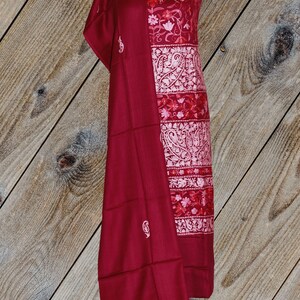 May include: A maroon shawl with white embroidery and a matching maroon dress with white and pink floral embroidery. The dress and shawl are displayed on a mannequin against a woodgrain background.